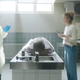A man and a woman stand around an autopsy table with a dead body on it.
